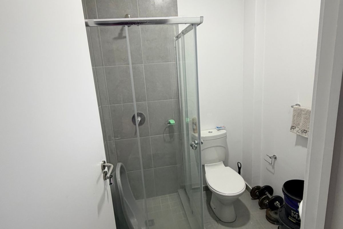 A compact bathroom featuring a glass-enclosed shower with grey tiling, a standard toilet, and tiled flooring.