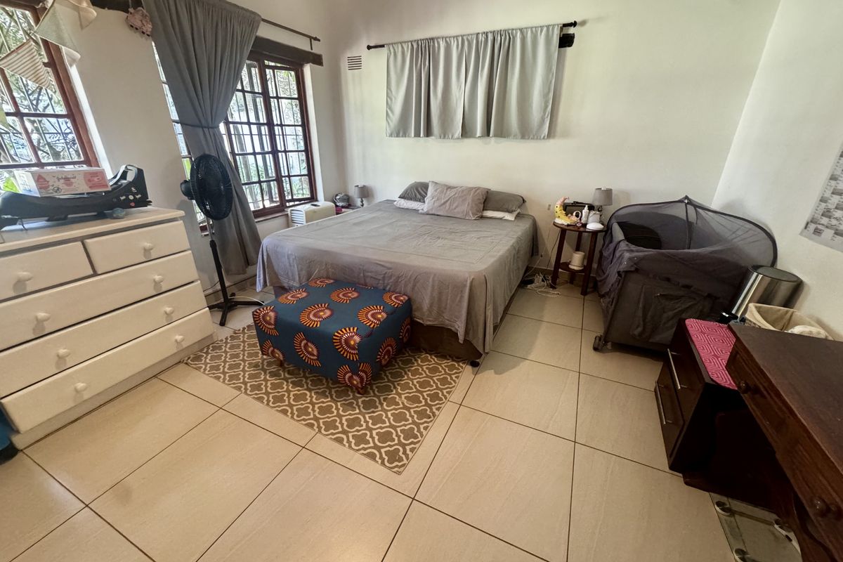 A bedroom featuring tiled flooring and large windows with security bars, providing natural light and a functional layout.