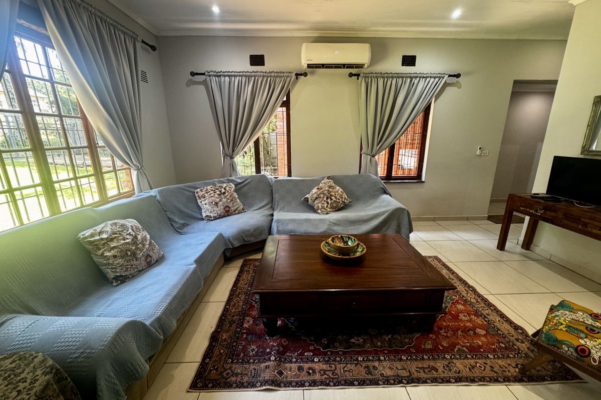 Spacious living room featuring large windows, tiled flooring, and a wall-mounted air conditioning unit, offering a comfortable and functional living space.