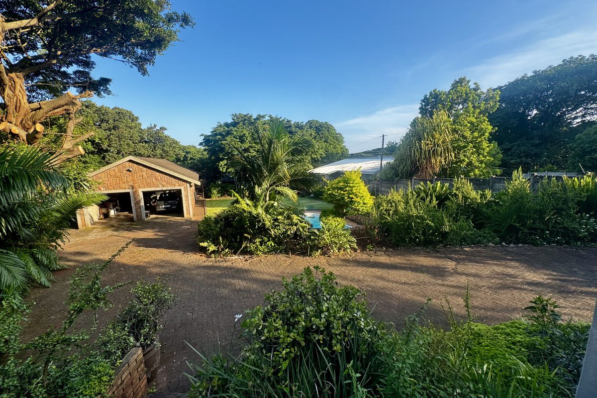 Spacious backyard featuring a paved driveway, a detached brick garage, established garden landscaping, and a swimming pool area.