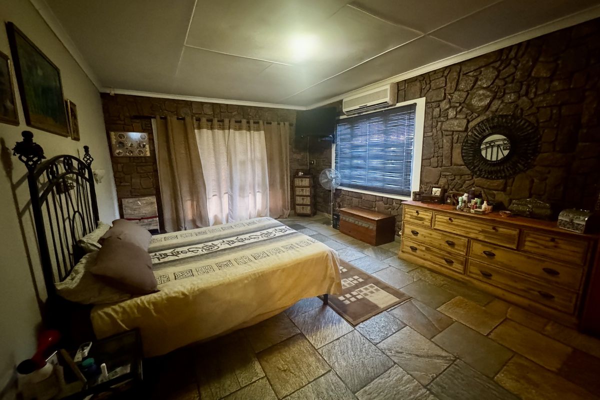 Spacious bedroom featuring rustic stone feature walls, natural stone flooring, and a wall-mounted air conditioning unit.