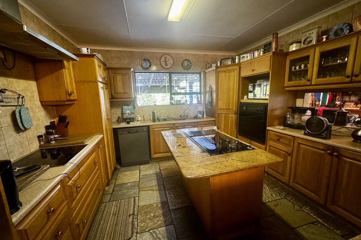 A traditional kitchen featuring wooden cabinetry, a central island with a built-in hob, stone-style flooring, and tiled splashbacks.