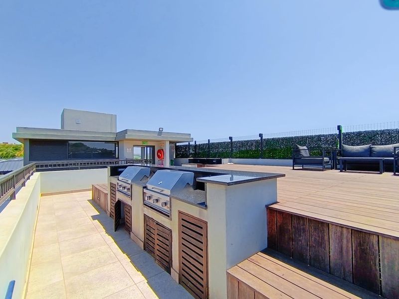 Spacious rooftop terrace featuring a built-in braai station with granite countertops, timber decking, and panoramic views, perfect for outdoor entertaining.