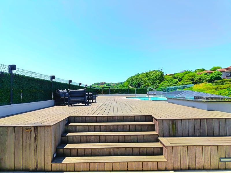 Spacious outdoor pool area featuring extensive timber decking, a swimming pool with glass balustrades, and scenic elevated views.