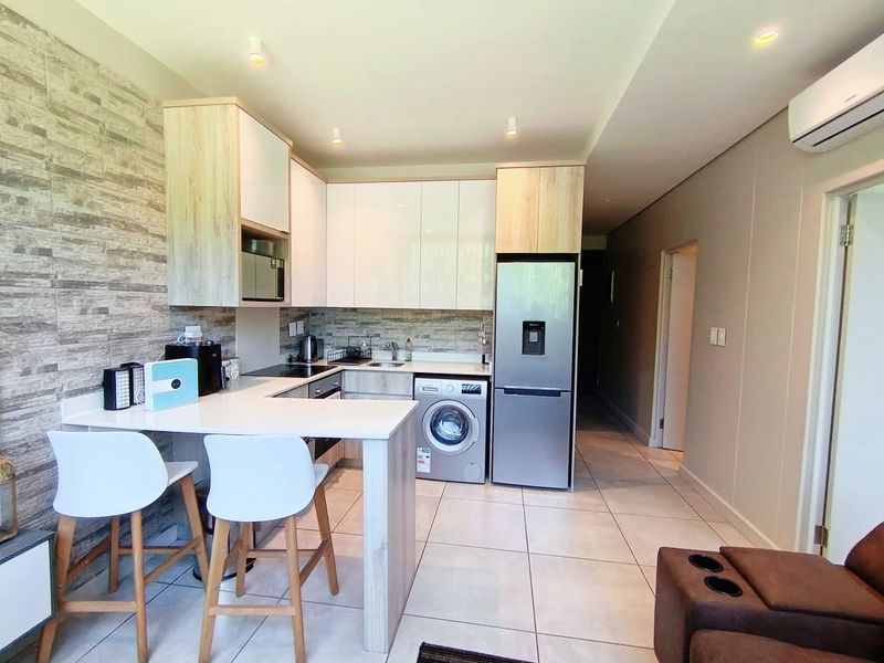 Modern open-plan kitchen featuring sleek cabinetry, stone countertops, integrated appliances, and tiled flooring, seamlessly flowing into the living area.