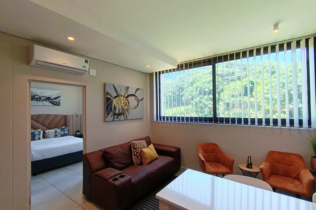 A well-lit living room featuring tiled floors, a wall-mounted air conditioning unit, and large windows with vertical blinds offering a pleasant green outlook.