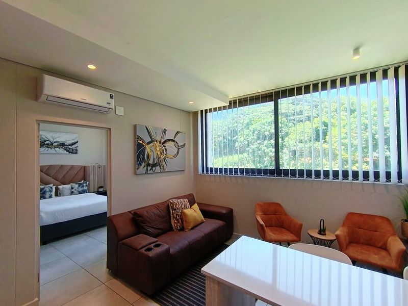 A well-lit living room featuring tiled floors, a wall-mounted air conditioning unit, and large windows with vertical blinds offering a pleasant green outlook.