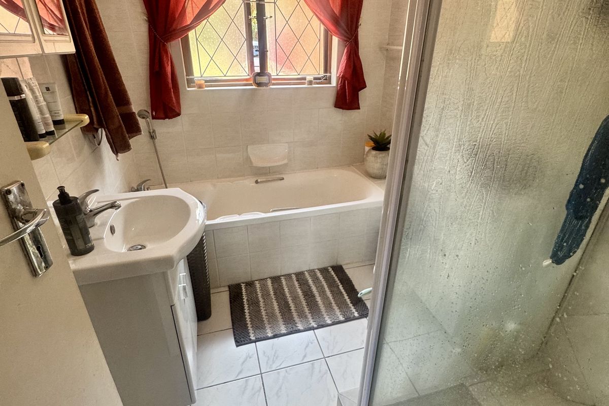 A functional bathroom featuring a built-in bathtub, a separate shower enclosure, and a vanity basin with tiled walls and flooring.