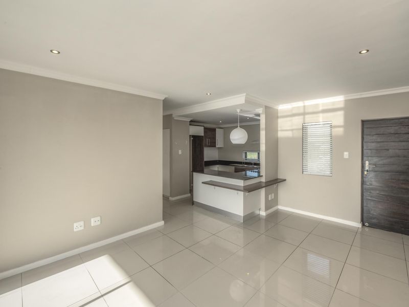 An open-plan living area featuring polished tile flooring, recessed lighting, and a functional kitchen with a breakfast bar and modern cabinetry.