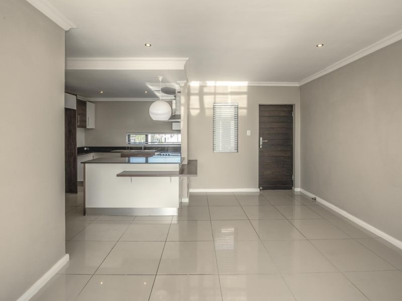 An open-plan living and kitchen area featuring neutral walls, large format floor tiles, recessed lighting, and a modern kitchen island with built-in cabinetry.