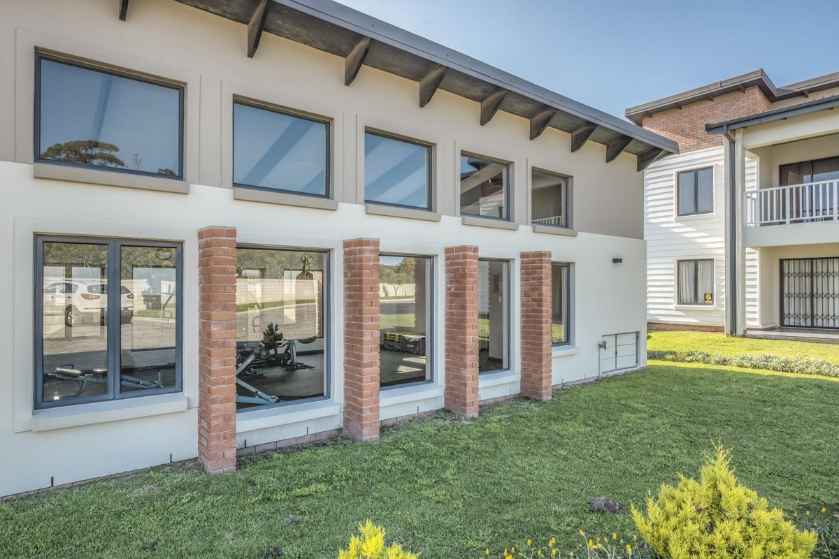 A modern apartment exterior featuring large windows, exposed brick architectural detailing, and well-maintained surrounding lawn area.