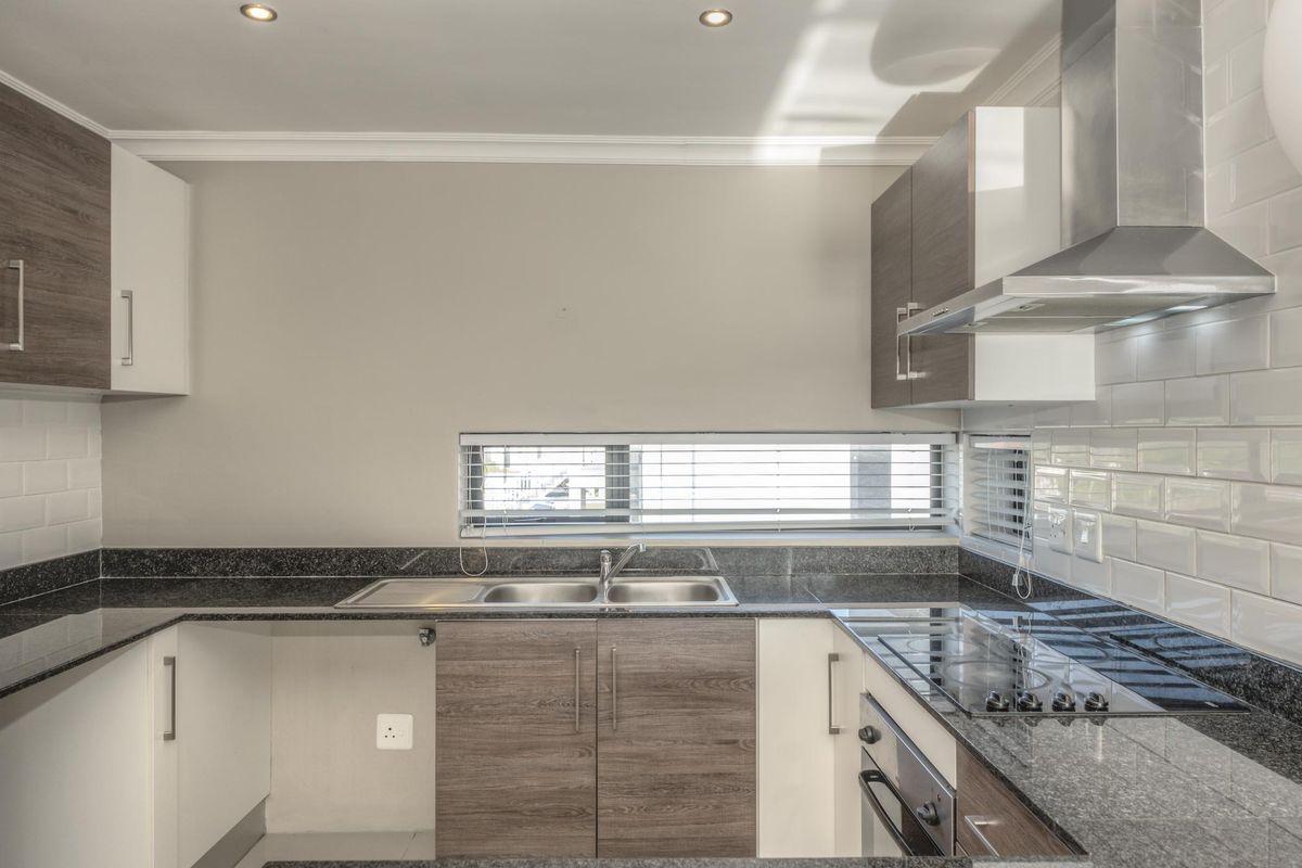 Modern kitchen featuring granite countertops, subway tile backsplash, built-in oven, electric hob, and stainless steel extractor fan with ample storage cabinetry.
