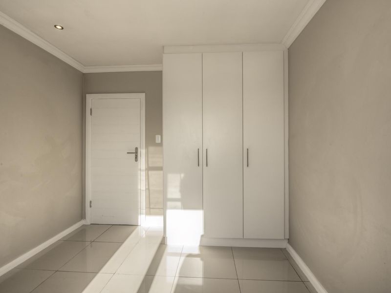 A bright, empty bedroom featuring neutral tiled flooring, built-in white wardrobes, and recessed ceiling lighting.