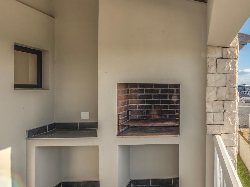 A covered balcony featuring a built-in brick braai, stone cladding accents, and tiled flooring, offering a functional outdoor entertainment space.
