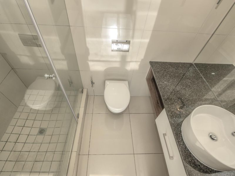 Modern bathroom featuring a glass-enclosed shower, wall-mounted toilet, and a sleek vanity with a granite countertop and vessel sink.