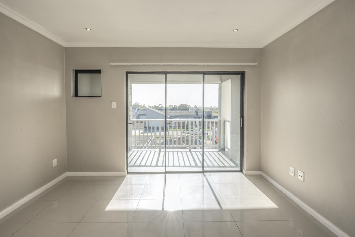 A bright, empty living area featuring neutral walls, tiled flooring, recessed lighting, and a large sliding glass door leading to a balcony.