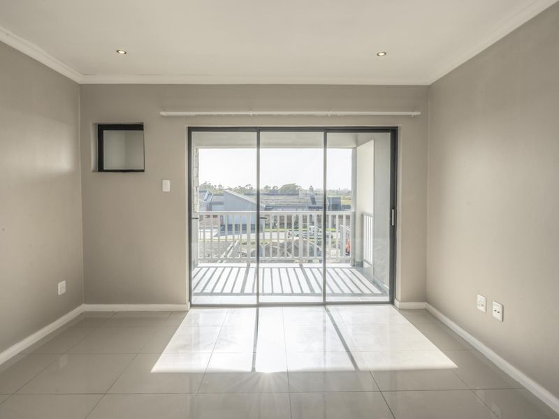 A bright, empty living area featuring neutral walls, tiled flooring, recessed lighting, and a large sliding glass door leading to a balcony.