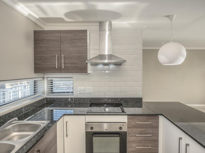 Modern kitchen featuring granite countertops, subway tile backsplash, built-in oven, electric hob, and stainless steel extractor fan with ample cabinetry.