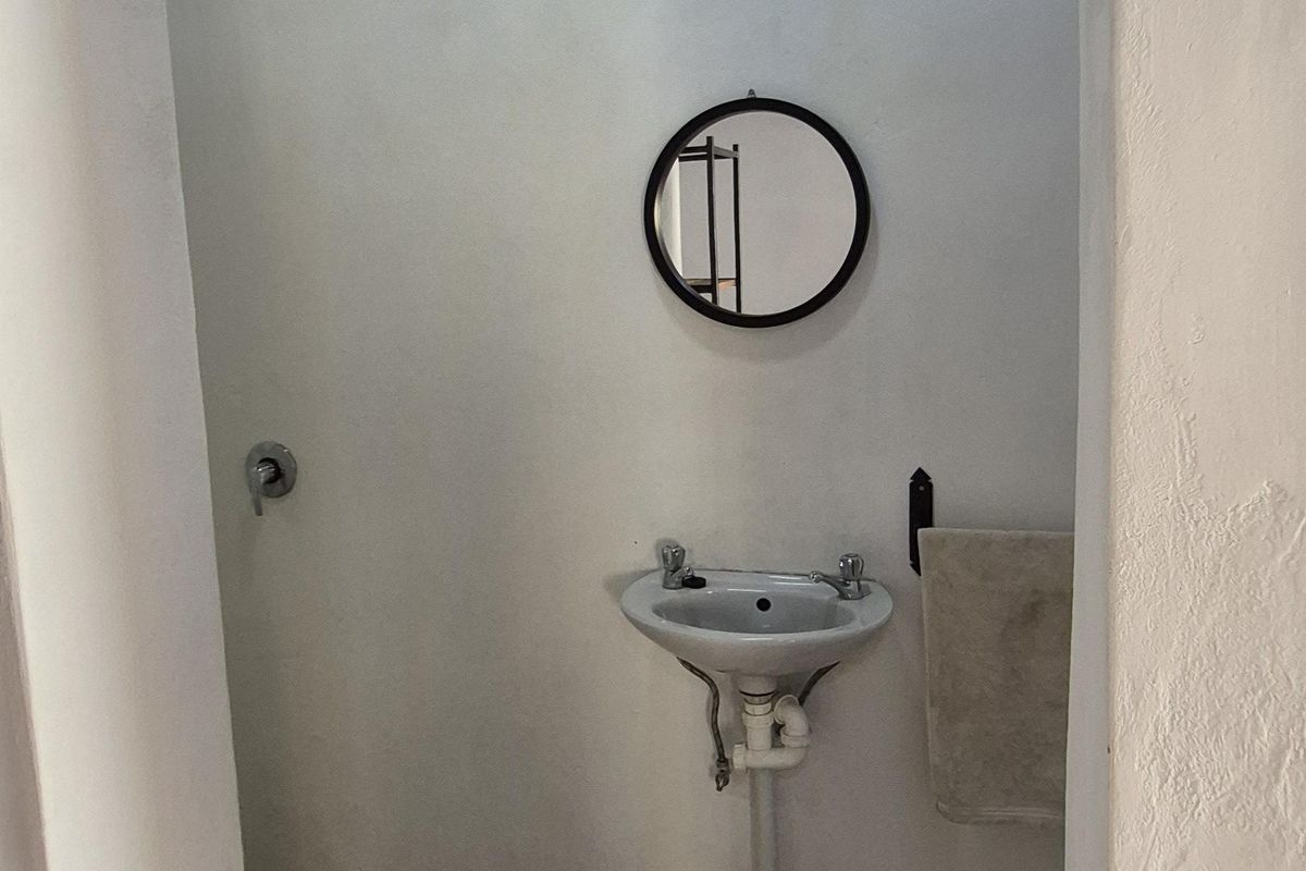 A compact bathroom featuring a wall-mounted basin, exposed plumbing, and a simple shower fixture with a rustic, unfinished aesthetic.