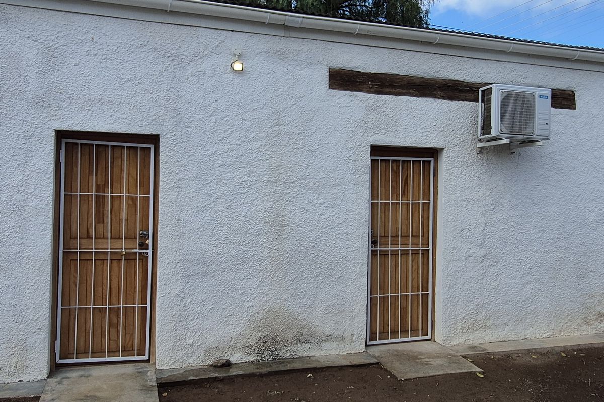 Exterior view of the rear building elevation featuring two wooden doors with security gates and a wall-mounted air conditioning unit.