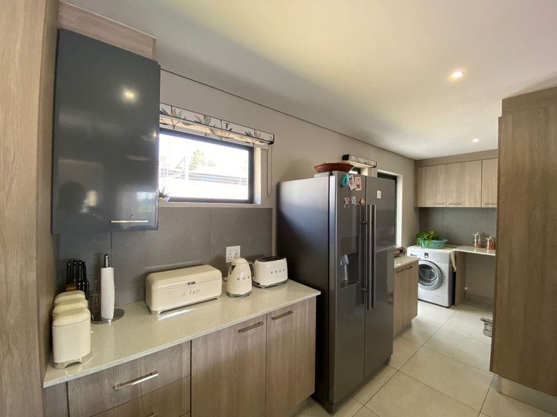 Modern kitchen featuring wood-finish cabinetry, stone countertops, and integrated laundry space with tiled flooring and recessed lighting.