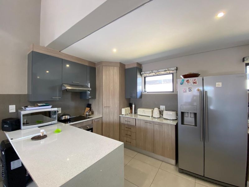 Modern kitchen featuring sleek grey and wood-tone cabinetry, stone countertops, integrated appliances, and recessed lighting in an open-plan layout.