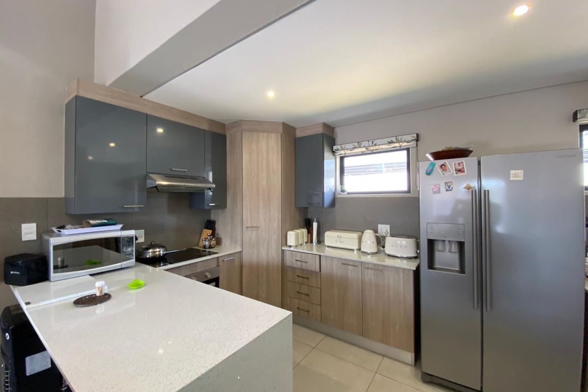 Modern kitchen featuring sleek grey and wood-tone cabinetry, stone countertops, integrated appliances, and recessed lighting in an open-plan layout.