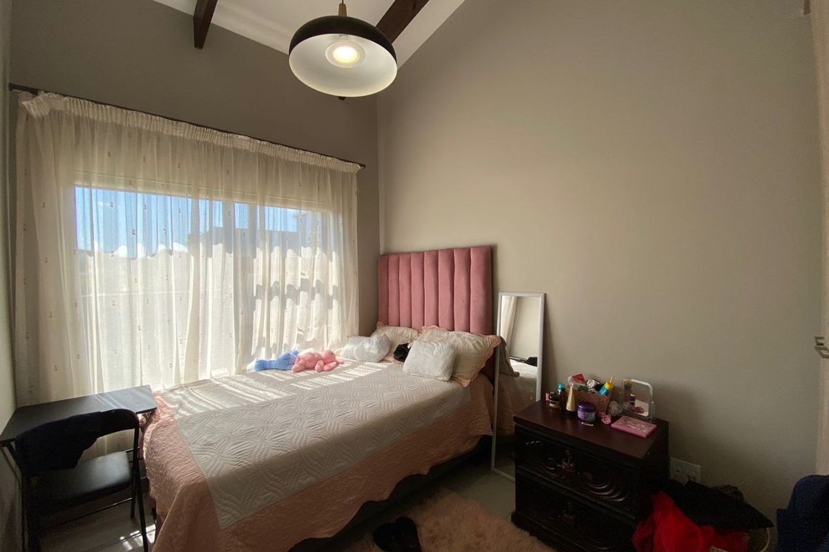 A well-lit bedroom featuring high ceilings with exposed timber beams and a large window allowing for ample natural light.