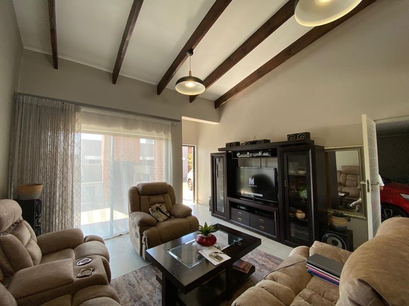 A living room featuring high vaulted ceilings with exposed timber beams, tiled flooring, and a sliding glass door providing access to the exterior.