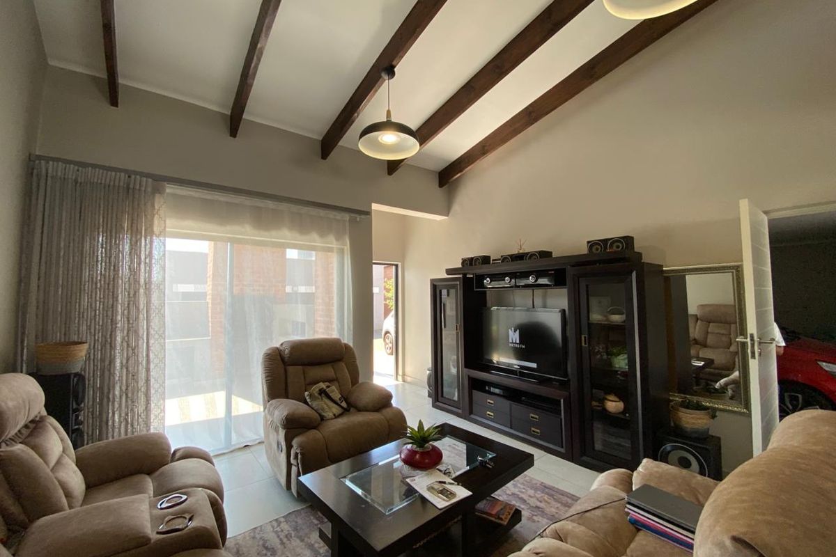 A living room featuring high vaulted ceilings with exposed timber beams, tiled flooring, and a sliding glass door providing access to the exterior.