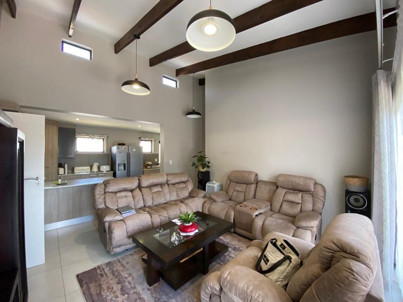 Spacious open-plan living area featuring high ceilings with exposed timber beams, pendant lighting, and a modern kitchen with integrated cabinetry.