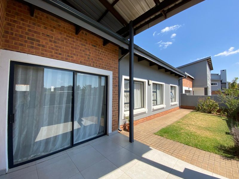 A covered patio area featuring tiled flooring and sliding glass doors, overlooking a neat garden with a paved walkway.