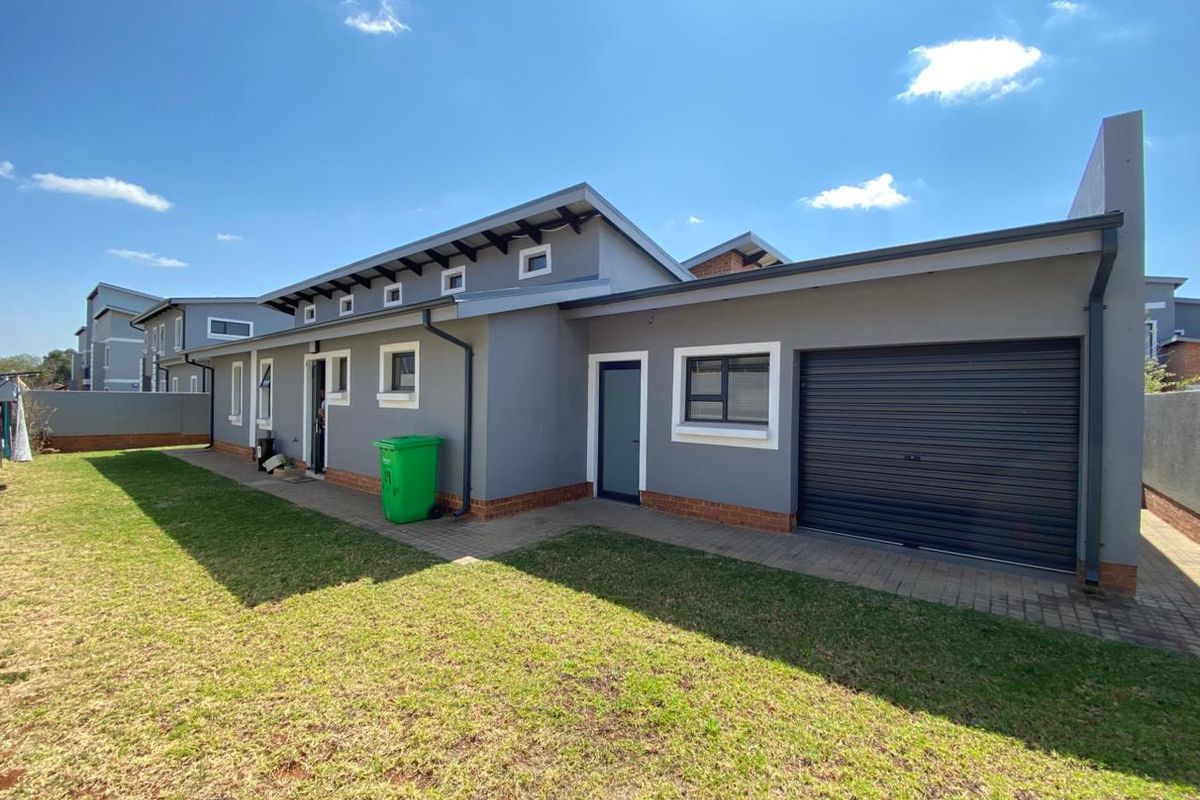 Rear view of the property featuring a paved walkway, roller garage door, and well-maintained exterior walls with clerestory windows.