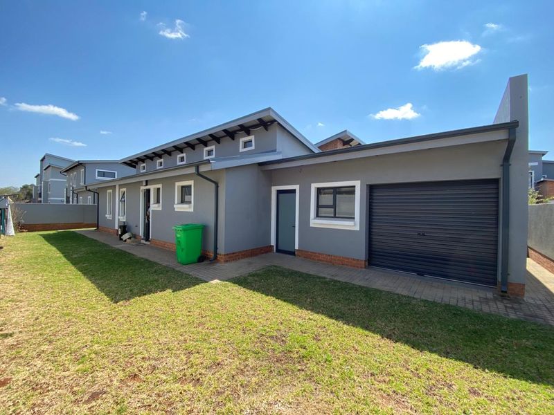 Rear view of the property featuring a paved walkway, roller garage door, and well-maintained exterior walls with clerestory windows.