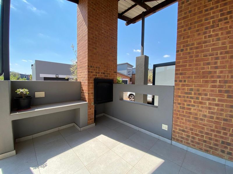 A covered patio area featuring a built-in braai, tiled flooring, and brick pillars, offering a functional outdoor entertainment space.