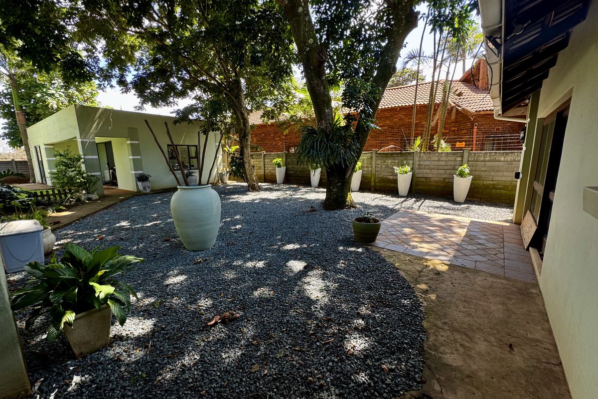 A low-maintenance rear garden featuring a gravel courtyard, mature trees, and a tiled patio area adjacent to the main dwelling.