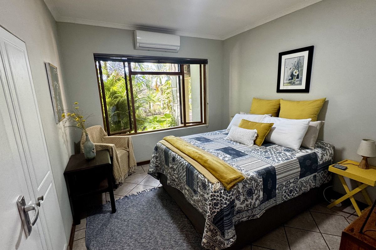 A well-maintained bedroom featuring tiled flooring, a wall-mounted air conditioning unit, and a large window overlooking the garden.