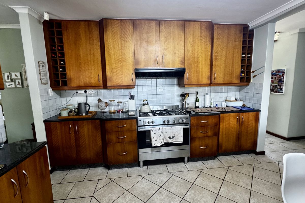 A functional kitchen featuring wooden cabinetry, a built-in extractor fan, a stainless steel gas stove, and tiled flooring.