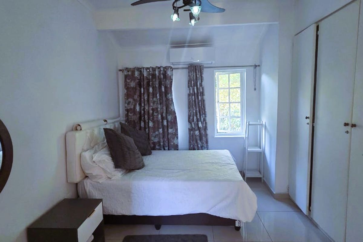 A functional bedroom featuring tiled flooring, built-in cupboards, a ceiling fan, and a wall-mounted air conditioning unit.