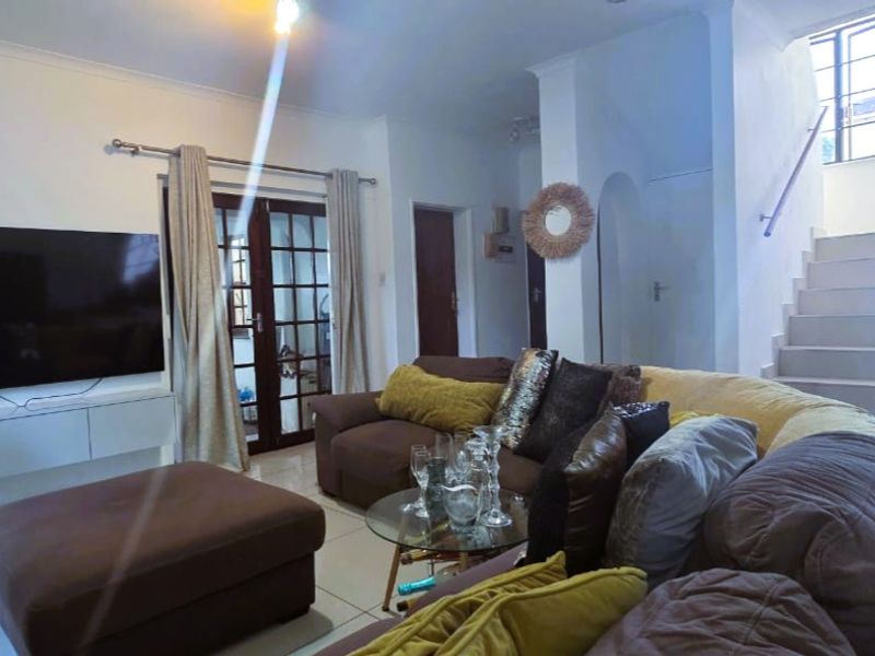 A comfortable living room featuring tiled flooring, a staircase leading to the upper level, and classic french doors providing natural light.
