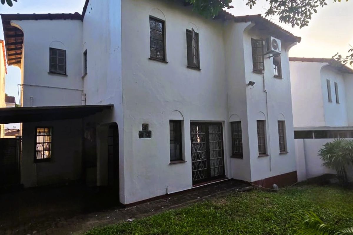 Rear view of a two-story townhouse featuring a covered patio area, security gates, and a small private garden space.