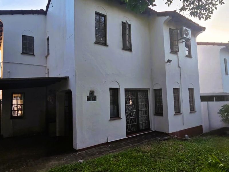 Rear view of a two-story townhouse featuring a covered patio area, security gates, and a small private garden space.