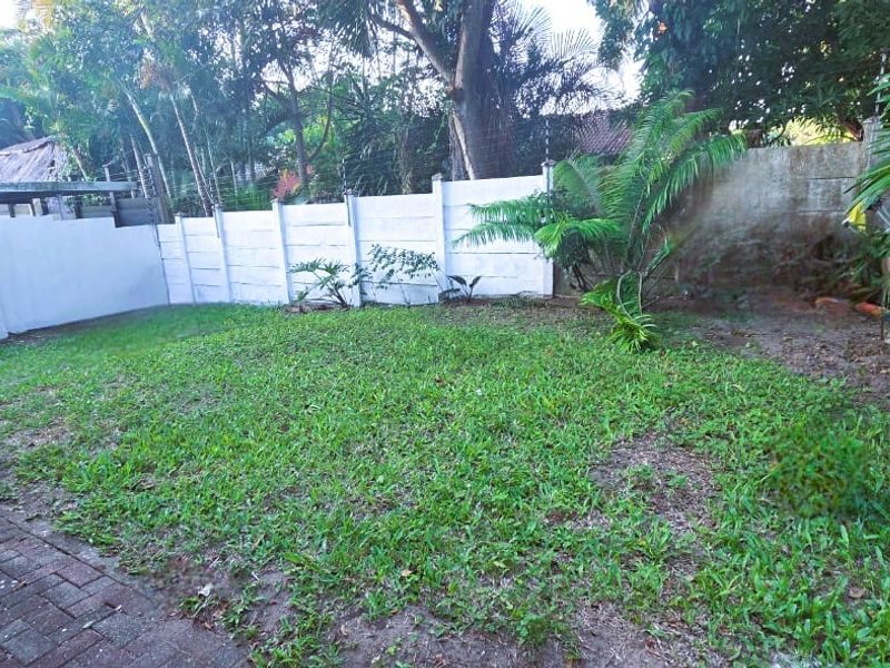 A private rear garden featuring a paved walkway, established trees, and a secure precast concrete boundary wall with electric fencing.