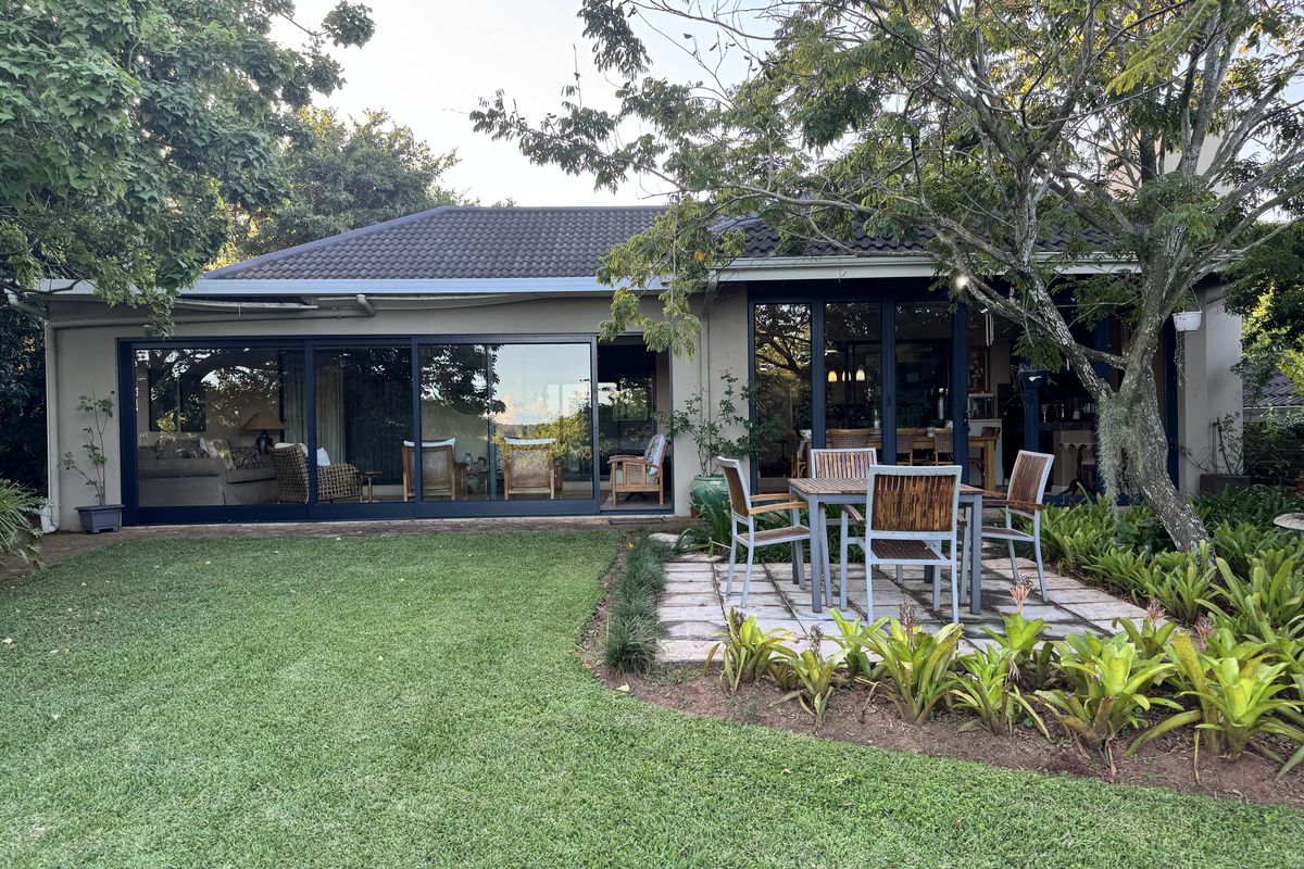 Rear view of the apartment featuring a paved patio, landscaped garden, and large sliding glass doors providing seamless indoor-outdoor flow.