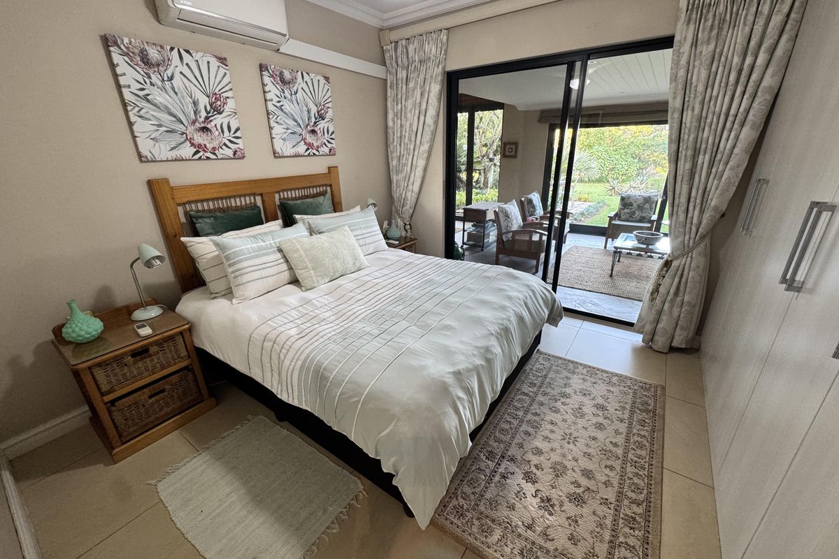 A well-maintained bedroom featuring tiled floors, built-in cupboards, a split-system air conditioner, and direct access to a private patio through sliding glass doors.