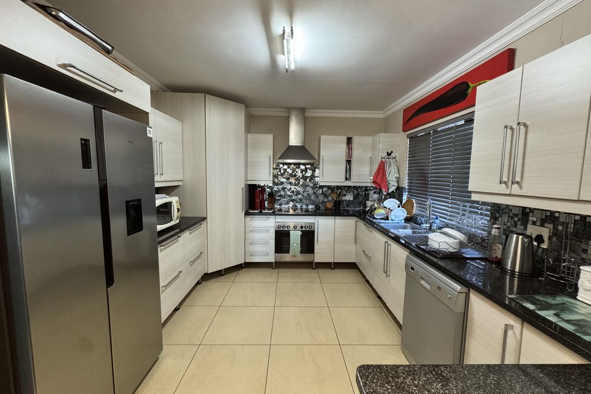 A functional kitchen featuring light wood-finish cabinetry, granite countertops, mosaic tile backsplash, and integrated stainless steel appliances with ceramic floor tiling.