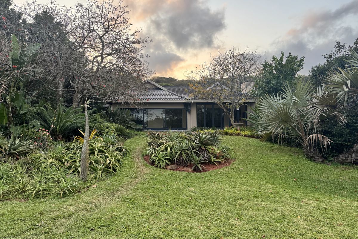 A view of the rear elevation of the property featuring a well-maintained garden, mature landscaping, and large sliding glass doors leading to the interior.