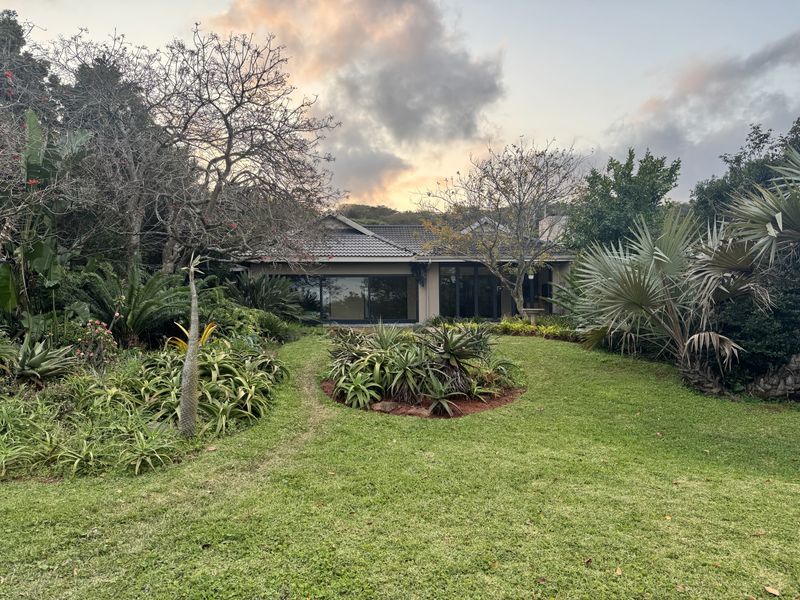 A view of the rear elevation of the property featuring a well-maintained garden, mature landscaping, and large sliding glass doors leading to the interior.