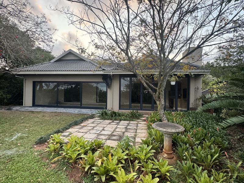 Rear view of the property featuring a tiled roof, large sliding glass doors, a paved patio area, and a mature landscaped garden.