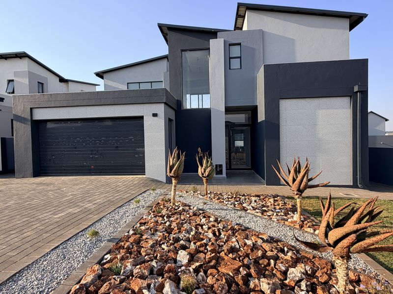 Modern double-story residential home featuring a contemporary facade, paved driveway, and a well-maintained landscaped rock garden.